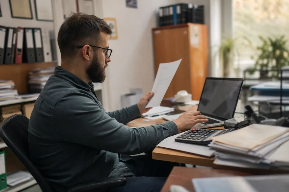 Księgowa porównuje numer konta z faktury na laptopie